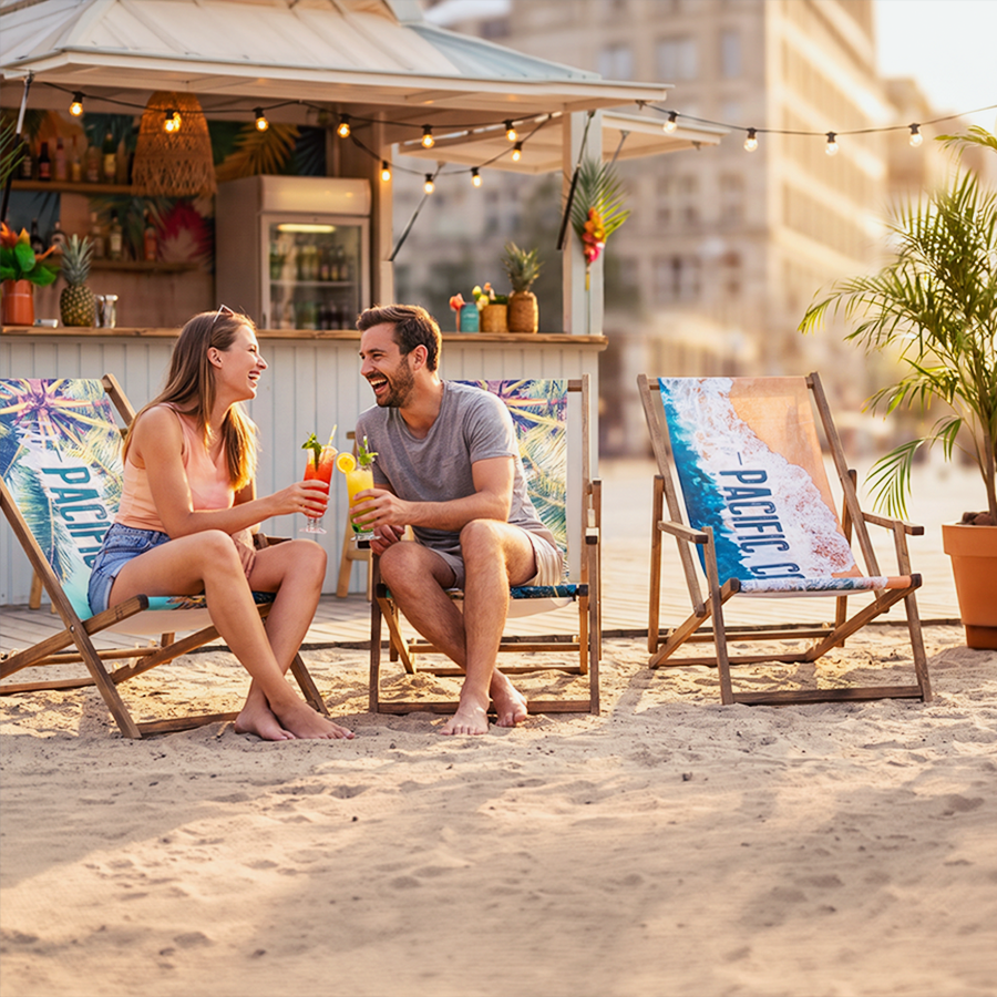 Ein Paar sitzt am Strand vor einer Bar in individuell bedruckten Liegestühlen