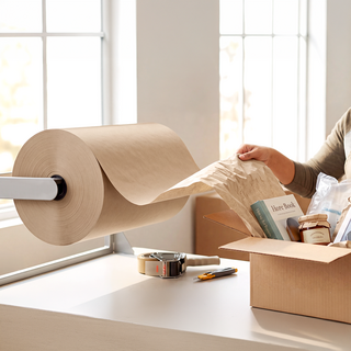 Eine Person nutzt Schrenzpapier auf Rolle an einem Packtisch