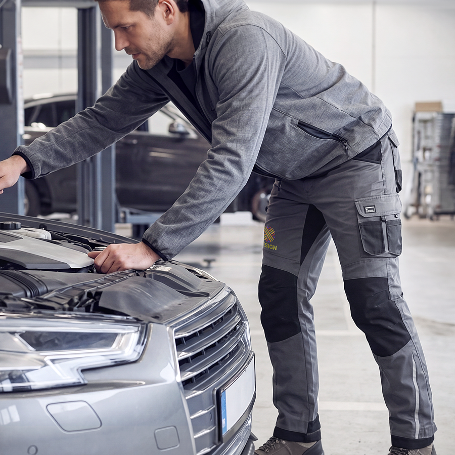 Ein Mann in bestickter Premium-Arbeitshose arbeitet an einem Auto